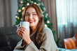 Happy asian woman holding coffee cup sit couch in house indoors with Christmas x-mas atmosphere decoration