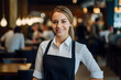 A portrait of a smiling young woman waitress in uniform inside a modern, stylish and bright restaurant. 