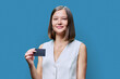 Young woman with bank credit card in hands on blue studio background