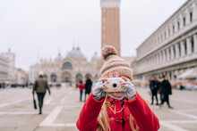 A Young Girl Focuses Through A Toy Camera, Capturing St. Mark's Basilica In The Backdrop Of A Cloudy Venice Day