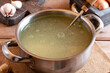 Saucepan with bouillon with a ladle on wooden table. Bone broth