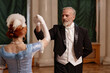 Waist up portrait of galant senior gentleman dancing with lady enjoying palace ball