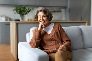 Carefree retirement. Happy senior caucasian woman sitting resting on couch at home and smiling to camera, free space