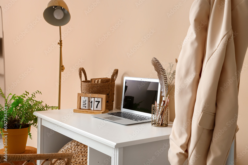 Modern laptop, stationery and decor on table near color wall