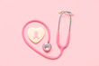 Heart shaped cookie with ribbon and pink stethoscope on color background. Breast cancer awareness concept