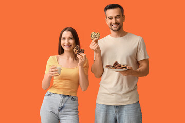 Canvas Print - Young couple with tasty cookies and glass of milk on orange background