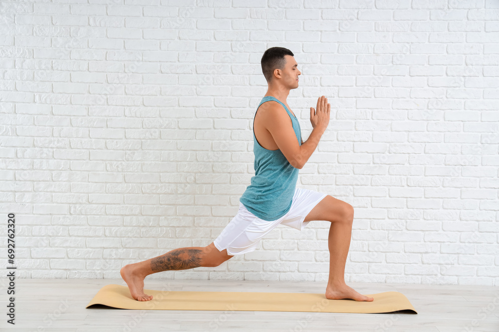 Young man doing yoga on mat near white brick wall