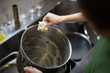 © Fotopogledi - Adult Woman Washes Cooking Pots by Hand in a Restaurant Kitchen Close Up Over the Shoulder View