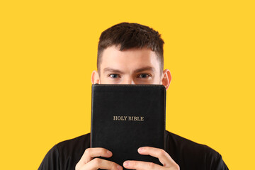 Young priest with Holy Bible on yellow background, closeup