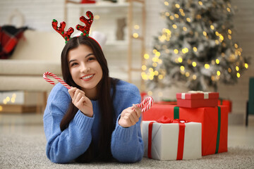 Canvas Print - Beautiful young woman in reindeer horns with candy canes at home on Christmas eve