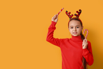 Wall Mural - Cute little girl in reindeer horns with candy canes on yellow background