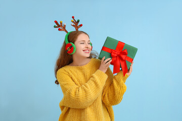 Wall Mural - Young woman in reindeer horns with Christmas gift on blue background