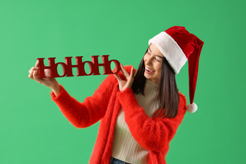 Poster - Young woman in Santa hat with Christmas greeting on green background