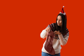 Poster - Young woman in Santa hat with Christmas sock on orange background