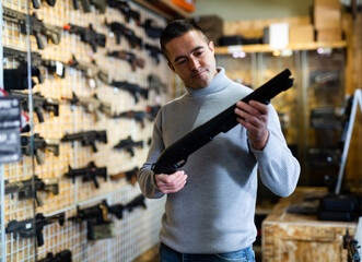 Sticker - Caucasian man choosing pump action shotgun in airsoft shop.