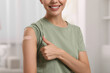 © New Africa - Woman with sticking plaster on arm after vaccination showing thumbs up at home, closeup