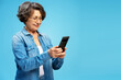 © Maria Vitkovska - Portrait smiling gray haired senior woman holding mobile phone shopping online, reading text message isolated on blue background. Technology concept