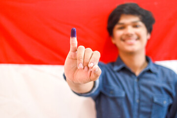 Young man showing finger after voting on Indonesia presidential election with Indonesia flag on the background, selective focus 