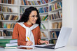 © Liubomir - Satisfied female student listens to an online lecture on a laptop, writes something in a notebook, sits at a table in an office, distance learning.