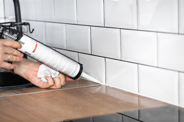 master of interior decoration, smears the joint of the tile and the kitchen countertop with white silicone instead of the skirting board, close-up