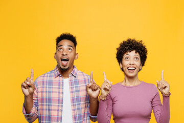 Wall Mural - Young surprised couple two friend family man woman of African American ethnicity in purple casual clothes together point index finger overhead on free area isolated on plain yellow orange background