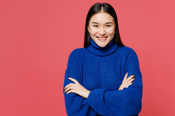Wall Mural - Young smiling happy woman of Asian ethnicity she wears blue sweater casual clothes hold hands crossed folded look camera isolated on plain pastel pink background studio portrait. Lifestyle concept.