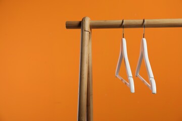 Empty clothes hangers on wooden rack against orange background. Space for text