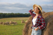 Beautiful woman near hay bale on farm. Space for text