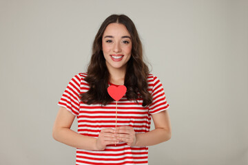 Poster - Beautiful young woman with paper heart on grey background