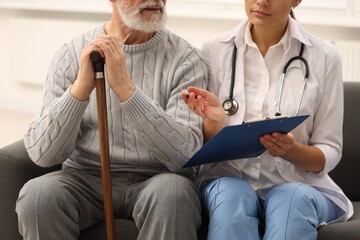 Poster - Nurse with clipboard assisting elderly patient on sofa indoors, closeup