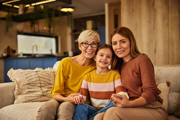 Wall Mural - Portrait of three generations, grandma, mother, and daughter, sitting on the couch, smiling for the camera.