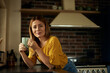 © bnenin - Portrait of a smiling woman, holding a cup of coffee, in the kitchen.