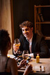 joyful man in elegant attire looking at girlfriend with glass of wine during date in restaurant