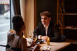 © LIGHTFIELD STUDIOS - happy man in elegant attire looking at girlfriend with glass of wine during date in restaurant
