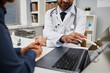 © Seventyfour - Cropped shot of male doctor showing information about treatment to patient using wireless laptop sitting at desk in clinic office