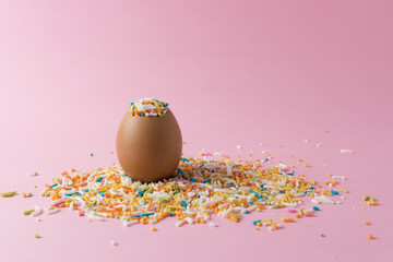 Egg with colorful sprinkles on pink background. Minimal Easter c