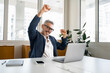 Enthusiastic mature businessman is clenching hands into fists, a happy senior business owner scream yes with triumph, having received great news of good deal, celebrating success of completed project