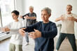 © Seventyfour - Medium full shot of senior male and female qigong class participants practicing tree pose for meditation