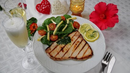 Sticker - Grilled swordfish steak with fresh salad, tomatoes and cheese on a plate rotating. Valentines day. Pour champagne into a glass. Close up