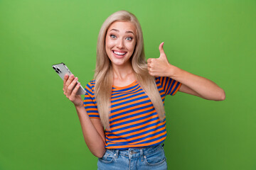 Poster - Photo of adorable optimistic girl wearing trendy clothes thumb up nice offer price gadget isolated on green color background