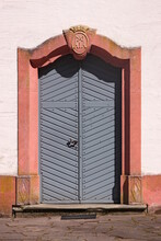 Grey Wooden Door In A Pink Baroque Sandstone Portal With An Old Keystone On The Facade Of Schankweiler Klause Church In Germany