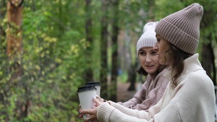 in autumn, two women walk through the park during the day, drinking coffee against the backdrop of a