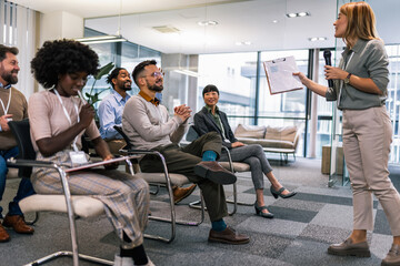 Young bussines woman lecturing her multiethnic colleagues. Having a speach while holding a microphone.