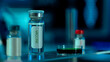 Close up of glass vial with vaccine and petri dish on table in research lab or hospital. Vials with clear liquid on blurred background. Concept of laboratory research, health care.