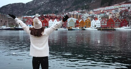 Wall Mural - A happy tourist woman enjoys the beautiful view of the Bryggen district in Bergen, Norway, during a cold winter day with snow