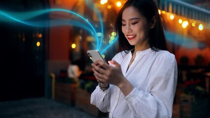 Wall Mural - Beautiful Smiling Asian Woman Using Smartphone on a City Street at Night. Wireless communication network concept. Mobile technology. Visualization of Information Lines Flying from Mobile Phone
