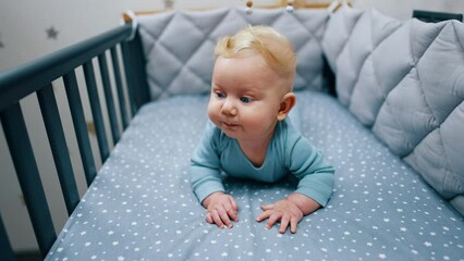 Sticker - Cute baby boy lies in his crib. Blue-eyed blond child looking around. Close up.