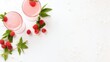  two glasses of raspberry smoothie with fresh raspberries on a white surface with green leaves and sprigs of raspberries on the side.