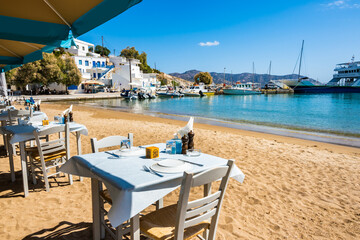 Wall Mural - Greek tavern restaurant with tables on beach in Kimolos port, Kimolos island, Cyclades, Greece