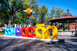 Colorful giant letters with Coyoacan words in front kiosk Hidalgo Park garden in Mexico City against blue sky and green trees on sunny day